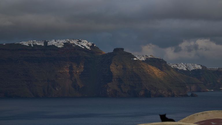 A cat sits on a domed roof in the town of Oia on the earthquake-struck island of Santorini, Greece, as the main town of Fira is seen in the background on Tuesday, Feb. 4, 2025. (AP Photo/Petros Giannakouris)