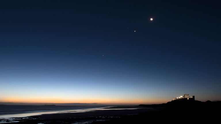 The Moon and Jupiter high over Bamburgh Castle in Northumberland, UK. This image was taken at first light of day with the Castle right of frame and the Farne Islands to the left.