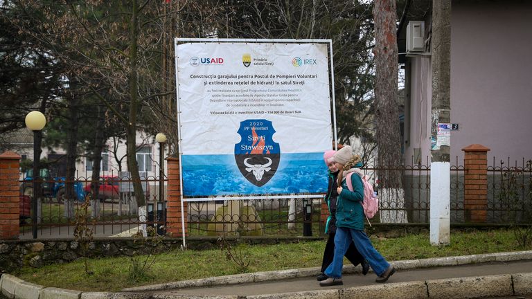 Children walk by a banner presenting a USAID supported project for the extension of the fire hidrants network in the village of Sireti, Moldova, Thursday, Jan. 30, 2025. (AP Photo/Aurel Obreja)