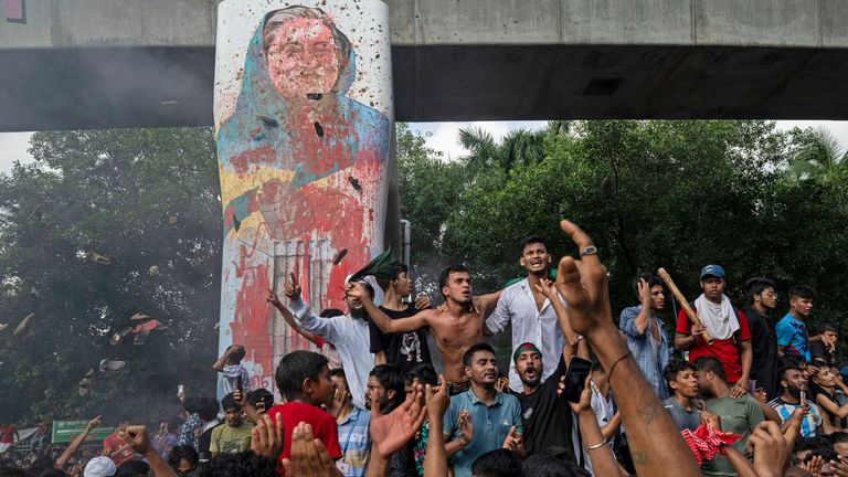 Protesters celebrate beside a defaced portrait of Ms Hasina.
Pic: Reuters/Fatima Tuj Johora