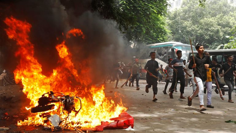 People pass in front of a vehicle burnt down by demonstrators during a rally against Ms. Hasina. Pic: Reuters / Rajib Dhar