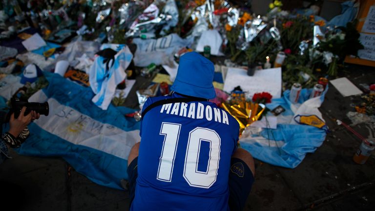 A fan mourns in front of flowers and posters left in tribute to Diego Maradona at the entrance of the Boca Juniors stadium known as La Bombonera in Buenos Aires, Argentina, Friday, Nov. 27, 2020. (AP Photo/Natacha Pisarenko)