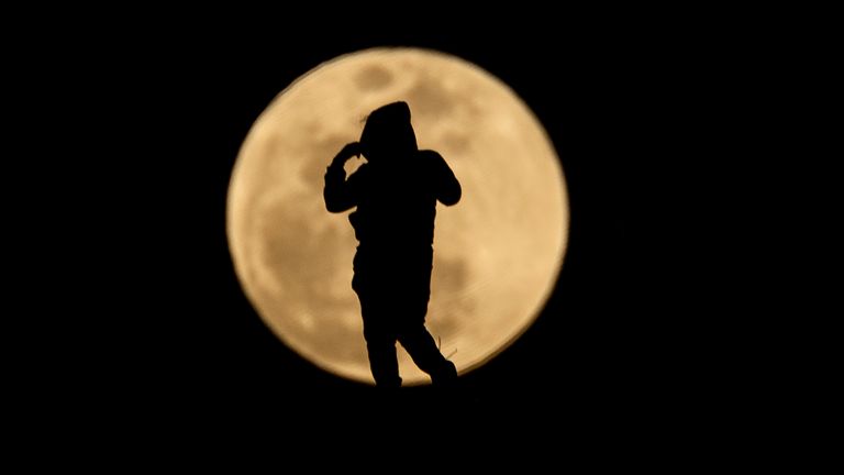 A person is silhouetted against the rising full moon in the evening sky, Thursday, March 14, 2025, in Los Angeles. The blood moon will occur later in the night, when a total lunar eclipse gives the moon a reddish hue. (Ringo Chiu via AP)