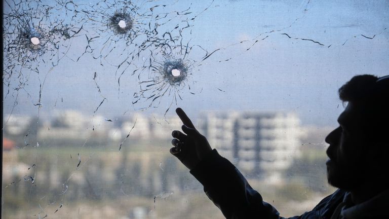 A nurse points to bullet holes in a window following the recent wave of violence between Syrian security forces and gunmen loyal to former President Bashar Assad, as well as subsequent sectarian attacks, at a hospital in the town of Jableh, in Syria's coastal region, on Monday, March 10, 2025. (AP Photo/Omar Albam)