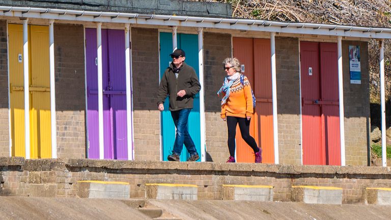 People walk past beach huts in sunny weather in Bridlington, Yorkshire.
Pic: PA