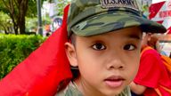 A boy with a Vietnamese flag while wearing a US army hat