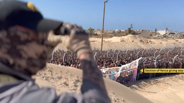 Mercenary guarding aid compound in Rafah signals a heart sign to the crowd, while a nearby section of fencing gives way under strain, 27 May 2025.
