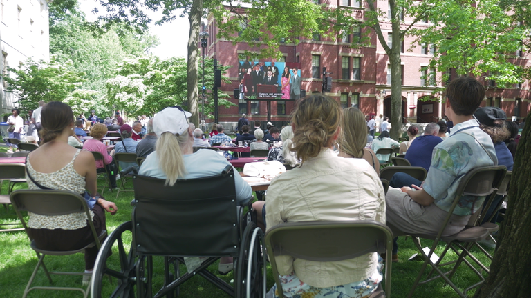 People watch the Harvard graduation ceremony from a nearby park