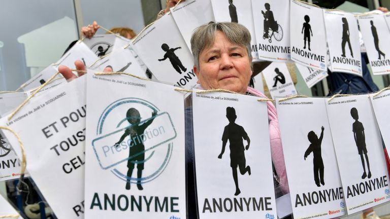 A woman peers behind a banner representing anonymous victims during a demonstration ahead of the verdict in the trial of Joel Le Scouarnec, a 74-year-old former surgeon, accused of raping and sexually assaulting 299 children, Wednesday, May 28, 2025 in Vannes, Brittany, western France. (AP Photo/Mathieu Pattier)