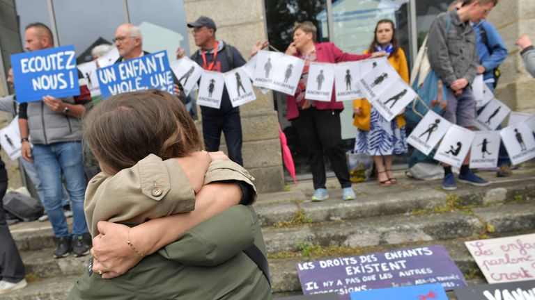 People hug as demonstrators hold a banner representing anonymous victims ahead of the verdict in the trial of Joel Le Scouarnec, a 74-year-old former surgeon, accused of raping and sexually assaulting 299 children, Wednesday, May 28, 2025 in Vannes, Brittany, western France. (AP Photo/Mathieu Pattier)