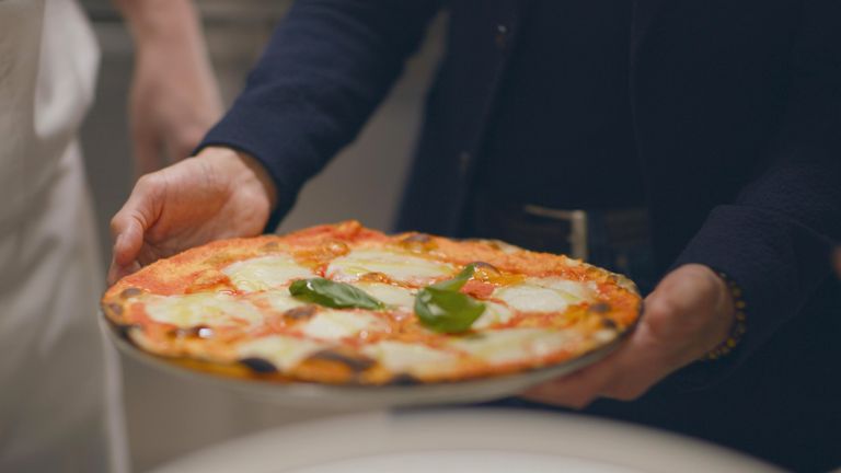 Ramadan El Sabawy hands Stanley Tucci a plate with his son's crispy Margherita Pizza. Pic: National Geographic
