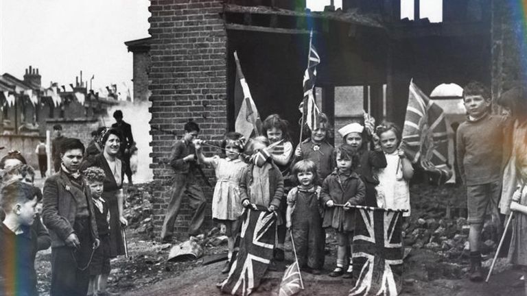 Children wave flags from the ruins of their homes in Battersea, south London. as they celebrate VE Day. Pic: PA