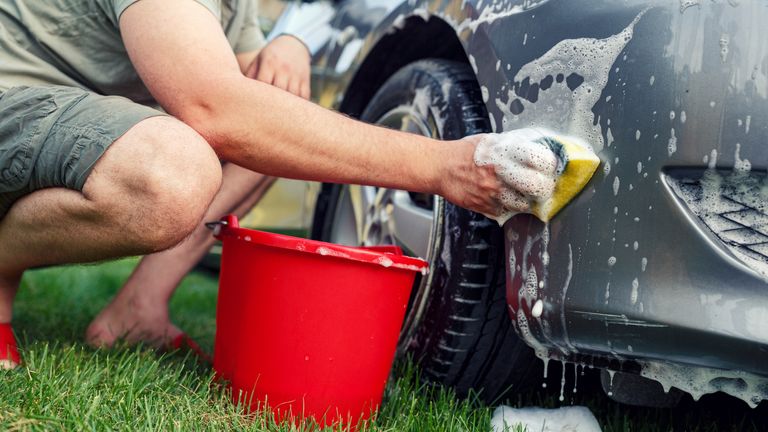 Sponge and bucket -Young male washing his car.
