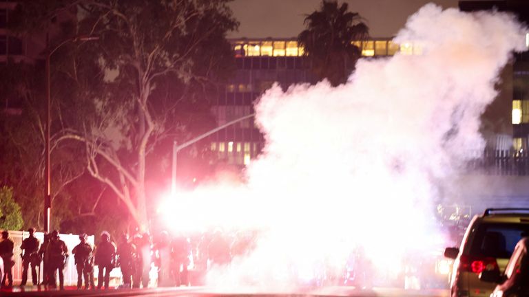 Polis Memurları, Los Angeles, California şehir merkezindeki federal göçmenlik taramalarına karşı bir protesto sırasında duman bölgeyi kapsadığı için bekçi olarak durur