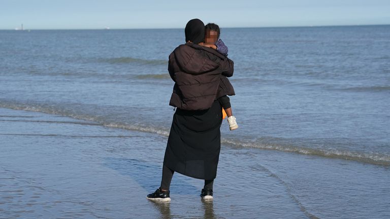 A young child is seen amongst a group of people thought to be migrants, waiting on the beach at Gravelines, France, to board a small boat in