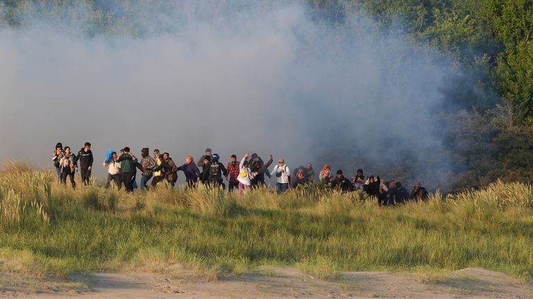 People thought to be migrants emerge from bushes on a beach in Gravelines, France, after French authorities had fired tear gas. Picture date