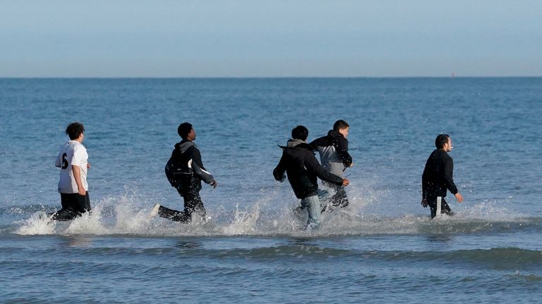 People thought to be migrants wade through the sea to board a small boat leaving the beach at Gravelines, France, in an attempt to reach the
