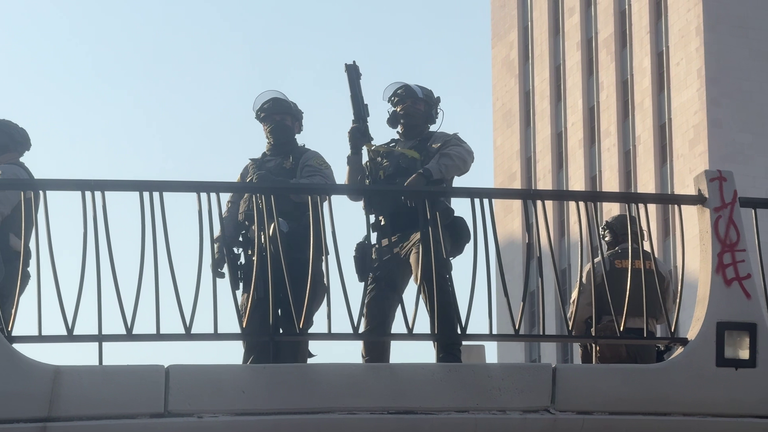 LAPD officers with crowd control weapons, in between aiming at protesters
