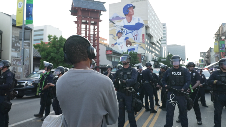 A protester faces LAPD in front of a mural of LA Dodgers baseball star Shohei Ohtani