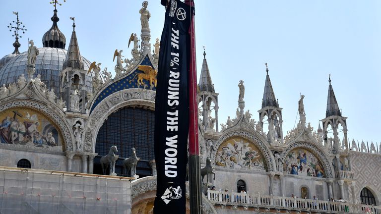An activist from Extinction Rebellion unfolds a banner in front of St. Mark's Basilica in Venice, Italy, on Thursday, June 26, 2025,  