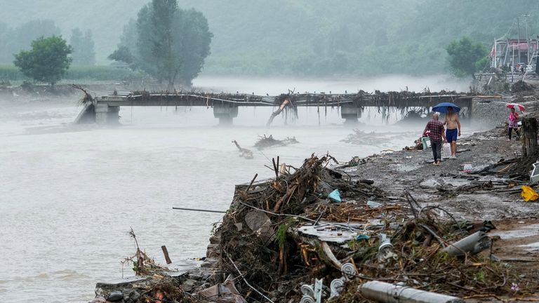 People walk by a damaged bridge after heavy rainfall flooded the area, in Huairou district of Beijing. Pic: Reuters