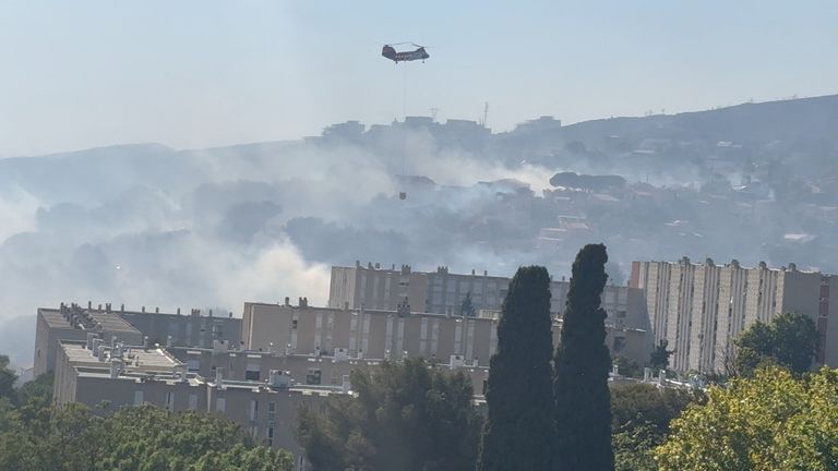 A helicopter carrying water, hovers over smoke from the wildfire in Marseille. Picture: Reuters