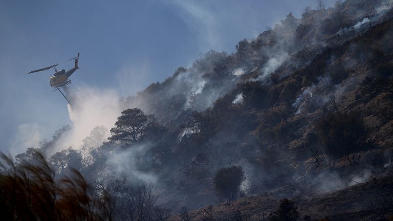 A firefighting helicopter makes a water drop during a wildfire in the town of Koropi, near Athens. Pic: Reuters
