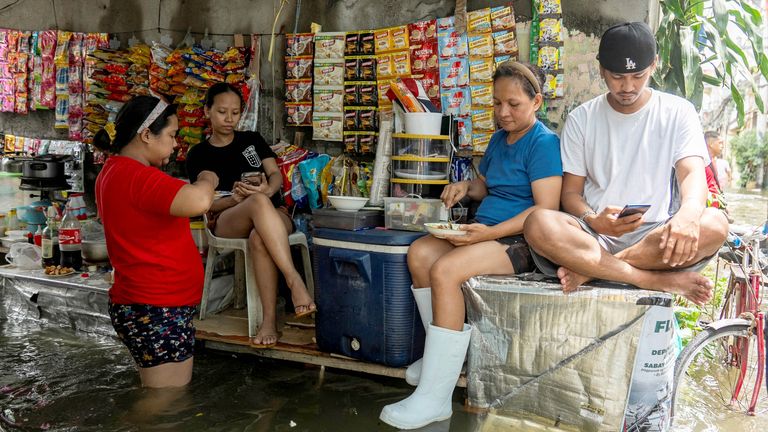 People rest at a sundry store along a flooded street following heavy rains brought by Typhoon Co-may in Navotas City, Metro Manila, Philippines, July 25, 2025. REUTERS/Lisa Marie David