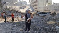 A Palestinian woman carries a child, as they inspect the site of an overnight Israeli strike on a house, in Gaza City, August 26, 2025. REUTERS/Ebrahim Hajjaj
