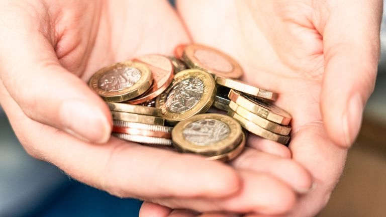 A woman holds a handful of UK pound coins and other British change. Pic: iStock