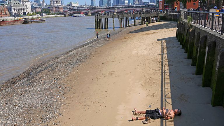 A man sunbathes on the beach along the River Thames in London as parts of the UK face a fourth heatwave of the summer. Pic: Kirsty Wigglesworth/AP