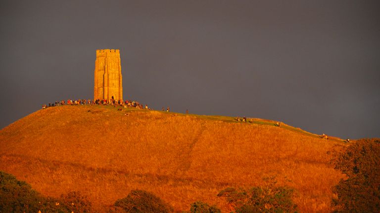 Akşamın erken saatlerinde güneş ışığı Somerset'te Glastonbury Tor'a çarpar, insanlar kan ayını görme umuduyla toplanır. Pic: PA