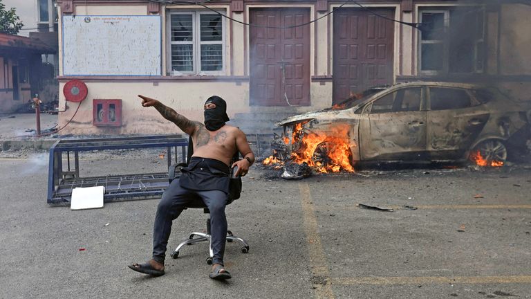 Bir gösterici, bu haftanın bozukluğu sırasında Yüksek Mahkemede yanan bir arabanın yanındaki bir sandalyeye oturuyor. Pic: Reuters