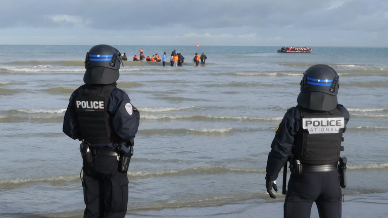 French police watch as migrants wait for a boat to pick them up