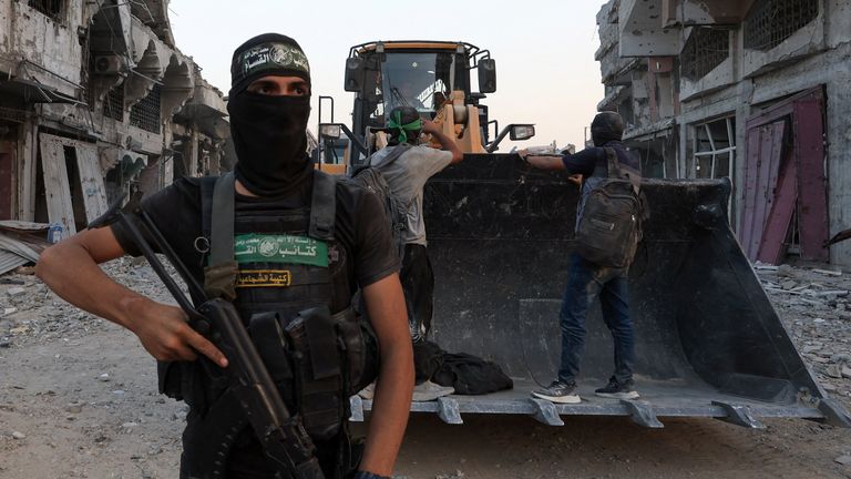 A Hamas militant stands next to heavy machinery moving covered human remains. Pic: Reuters