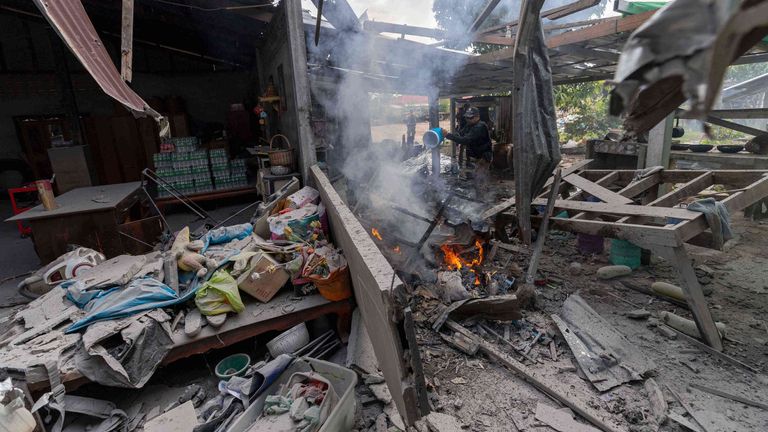 A Thai police officer splashes water to control fire at a house which, Thai local security forces say, was damaged by a Cambodian artillery strike in Surin province, Thailand, on 11 December. Pic: AP