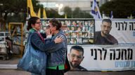 Israeli women hug in front of a banner with photos of former hostages, including Israeli police officer Ran Gvili. Pic: Reuters
