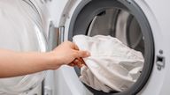 Individual is removing a clean white shirt from a washing machine, highlighting the laundry process in a bright and organized laundry room space