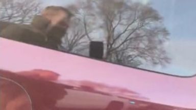 An ICE officer can be seen filming in a reflection.