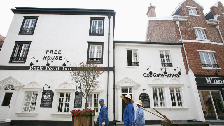 Gardeners walk near a replication of the Rock Point Inn and Cob Gate Fish Bar copied from Lyme Regis in Dorset, southwest England, at Shanghai's Thames Town in this September 25, 2006 file photo. Photo taken on September 25, 2006. To match feature Life China Thames. REUTERS/Nir Elias (CHINA)