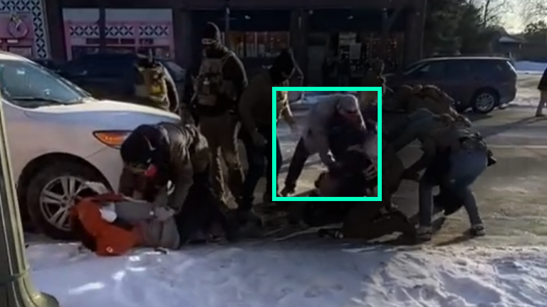 Still shows man in grey jacket search Alex Pretti's waistband 