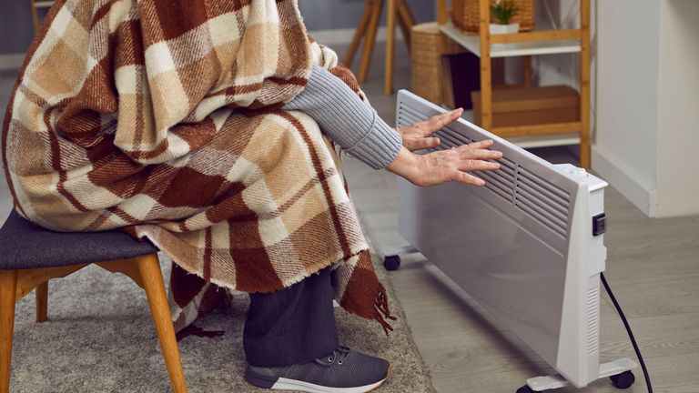 A cold man heats up his hands on an electric radiator. Pic: PA