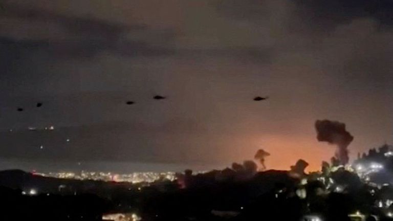 Helicopters, believed to belong to the US, fly past plumes of smoke rising from explosions, in Caracas, Venezuela. Pic: Reuters