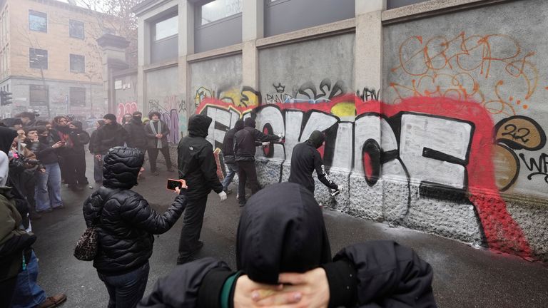 Outside, student protesters spray paint anti-ICE messaging on a wall. Pic: AP