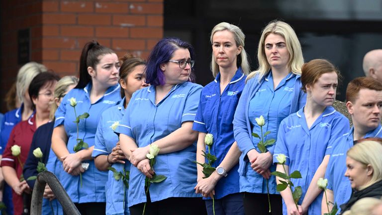 Nurses and medical workers hold single white roses outside Ms Doherty's funeral on Thursday. Pic: PA