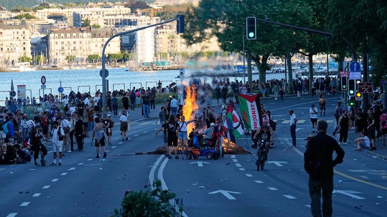 Protesters and others watch as a fire burns in the street during a demonstration in Geneva, Switzerland, ahead of the G7 summit. Pic: AP