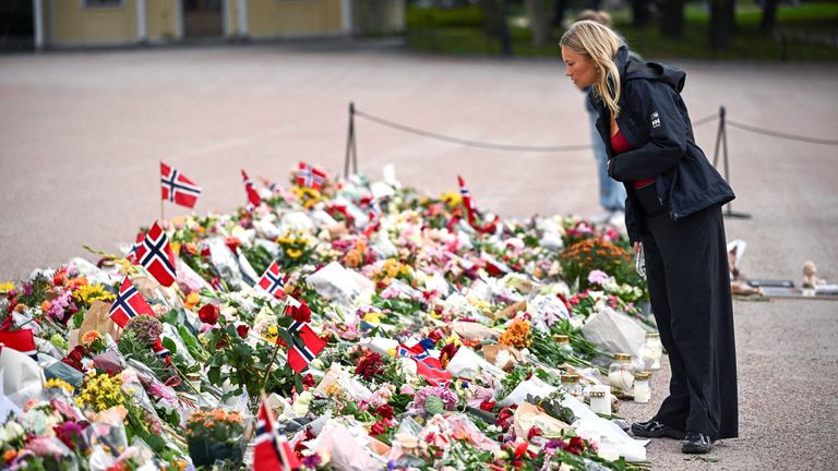 A woman stands near flowers and Norwegian flags placed outside the Royal Palace. Pic: Reuters